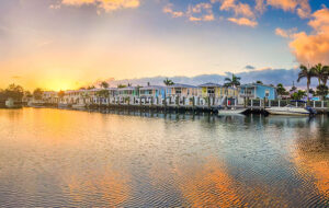 row of multi colored cottages along docks with rippling water reflecting sunset sky at key west feature
