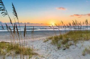 sunset over beach with orange and blue sky waves and sand dunes with sea oats and grass for amelia island destination feature