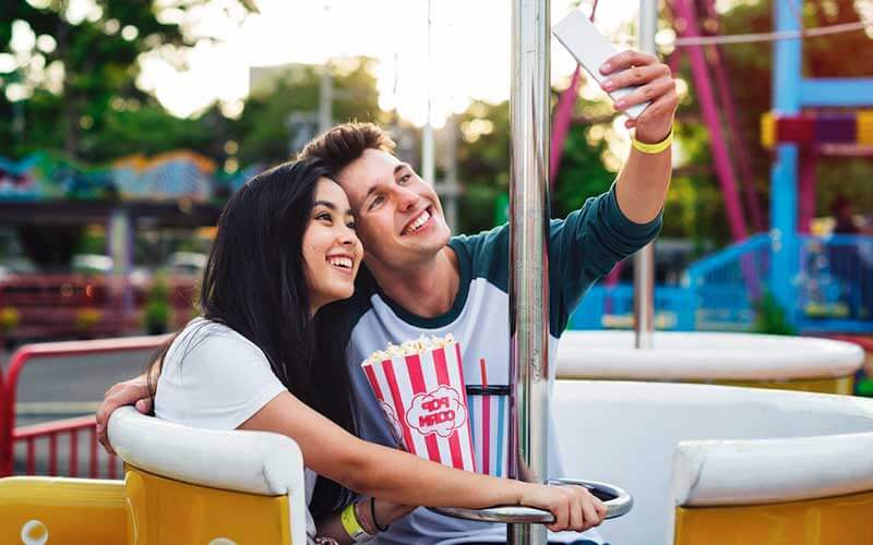 young couple dating at amusement park on ride with selfie and popcorn from where find affordable tickets