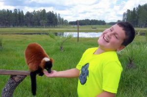 boy laughs while feeding lemur in a field with trees in the background at safari wilderness ranch lakeland
