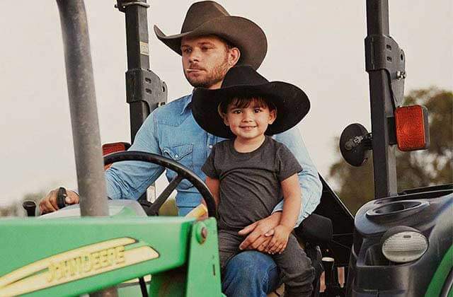 father and son with cowboy hats sitting on a tractor for cavenders western wear orlando