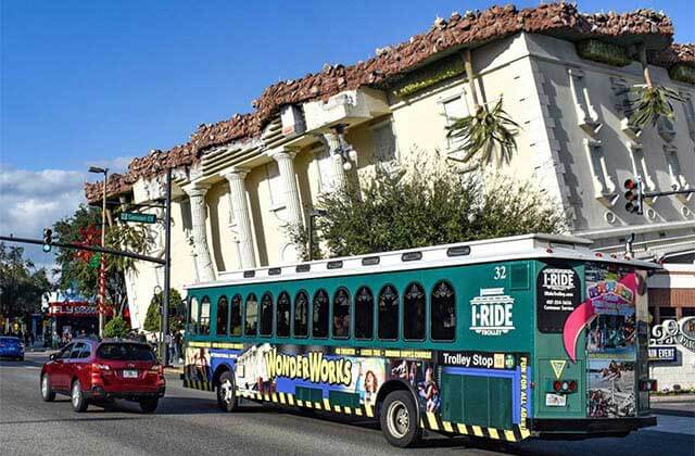 green trolley driving past wonderworks upside down building for i-ride trolley orlando