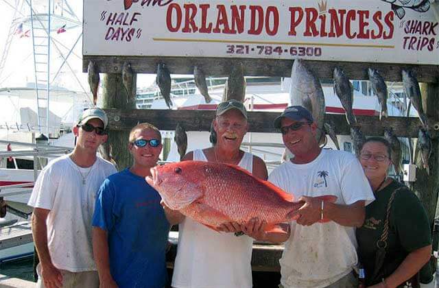 group of five holding a large red fish on the dock at princess fishing fleet cape canaveral