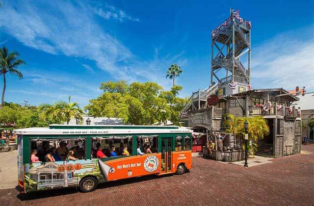 orange and green trolley bus parked at wooden structure with viewing tower at historic tours of america key west