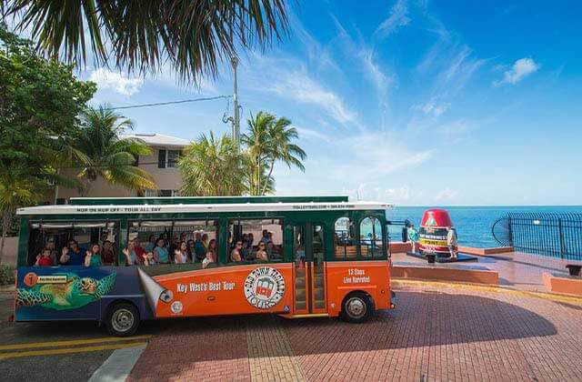 southern most point marker with orange and green trolley bus nearby at historic tours of america key west