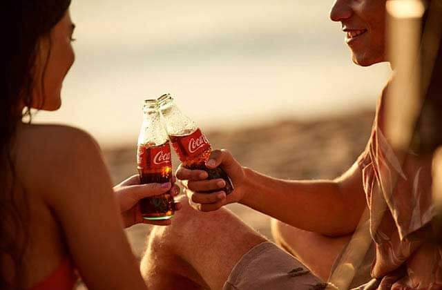 couple on the beach clinking coca cola bottles for coca cola store at disney springs