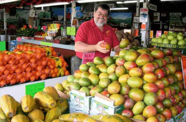 man smiling and holding mango at a fruit stand with different native fruits at historic redland tropical trail