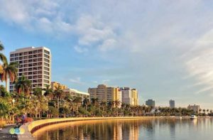 row of condos hotels and palm trees along sea wall with boat on inlet and cloudy sky at city of west palm beach destination feature