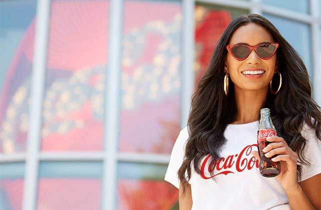 woman with brand sunglasses and shirt drinking a coke with the store behind at coca-cola store at disney springs