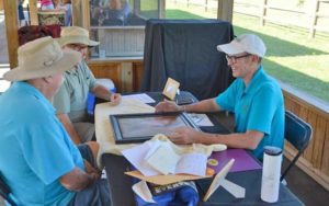 antique appraisers sitting at a table in a booth with painting