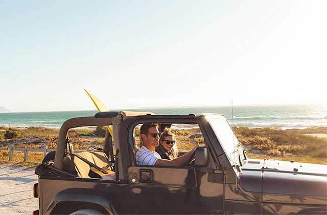 couple in a jeep with a surf board driving along coastal road at daytona area beaches