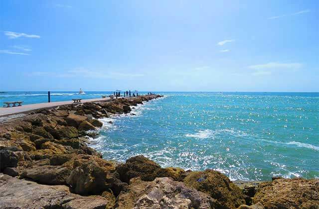 rocky shoreline with jetty with people looking out over blue waves at st lucie beaches florida
