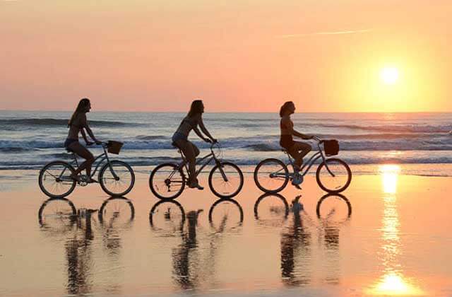 women bicycling on a beach at sunset at daytona area beaches