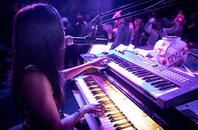 young lady playing two keyboards while singing into microphone with crowd at howl at the moon orlando