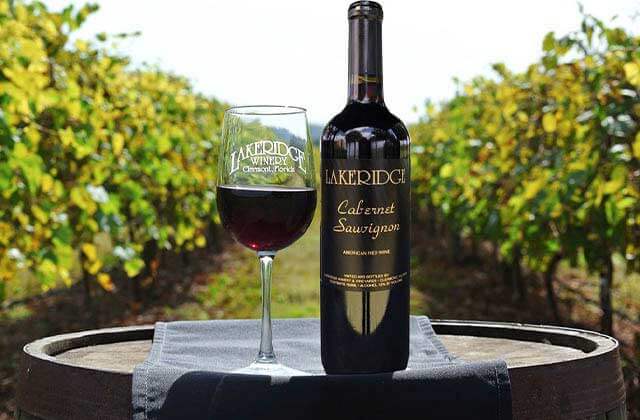 brand bottle and wine glass on a barrel with rows of vineyard at lakeridge winery vineyards orlando