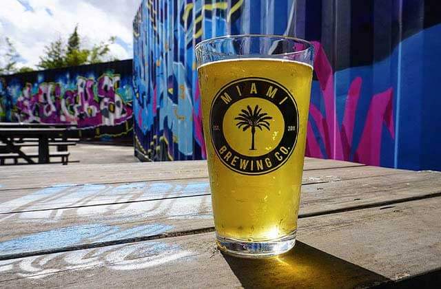 brand glass of draft beer on a picnic table near a fence with graffiti at miami brewing company