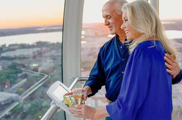 elderly couple with champagne looking out window of observation wheel capsule at the wheel at icon park orlando