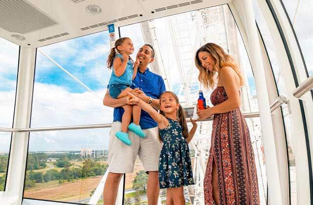 family of four standing in capsule with skyline behind at the wheel at icon park orlando