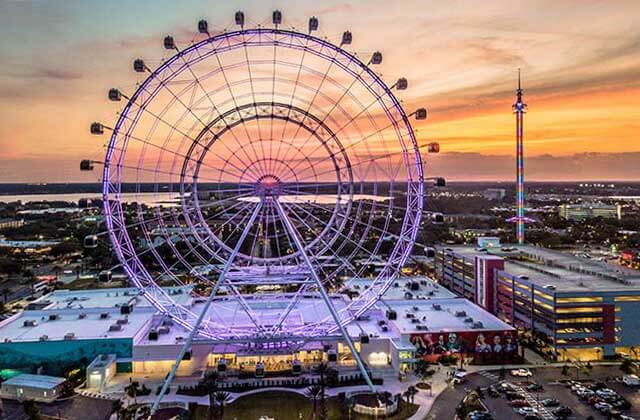 sunset view of observation wheel with purple lights at the wheel at icon park orlando