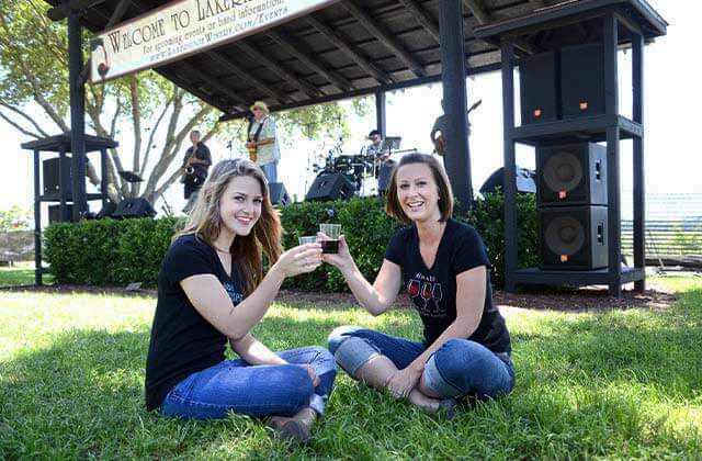 two young ladies toasting wine glasses with a band playing on stage at lakeridge winery vineyards orlando