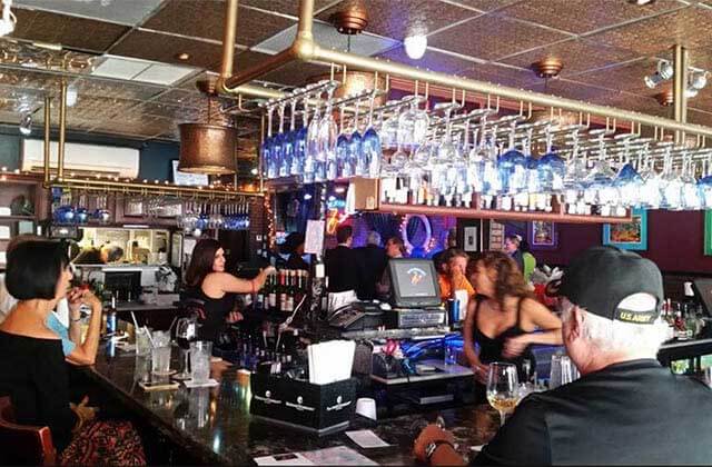 crowded bar area with stemware glasses on a rack hanging from the ceiling at blue jean blues fort lauderdale