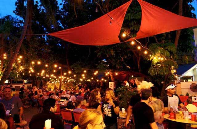 crowded outdoor dining area at night with string lights and red shades at viva argentinean steakhouse key west
