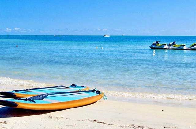 a pair of paddleboards on the beach with jet skis moored in the background at barefoot billys key west