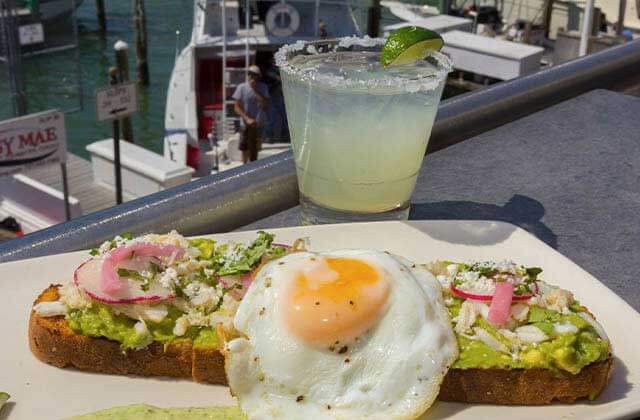 plate of avocado toast with egg and margarita with view of dock and boats at marina cantina tequila bar grill clearwater