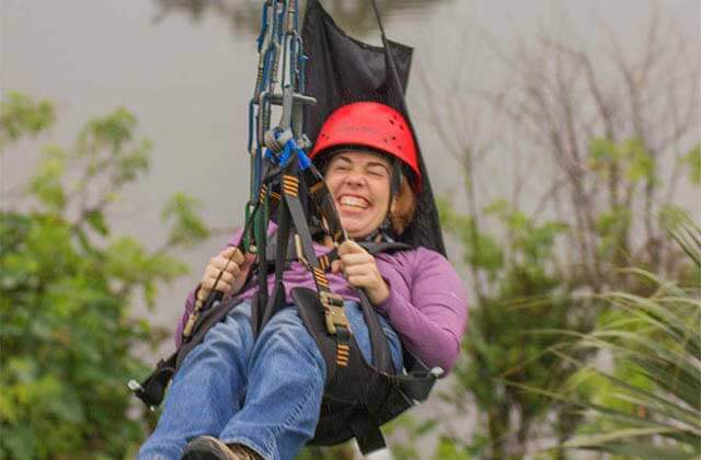 woman smiles while ziplining in a disability adaptive harness at zipline stompin gator off road adventure gatorland