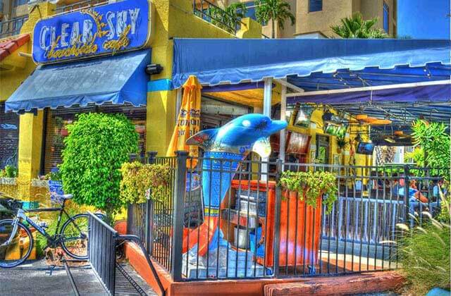 yellow and blue exterior of restaurant with patio and dolphin statue at clear sky beachside cafe clearwater