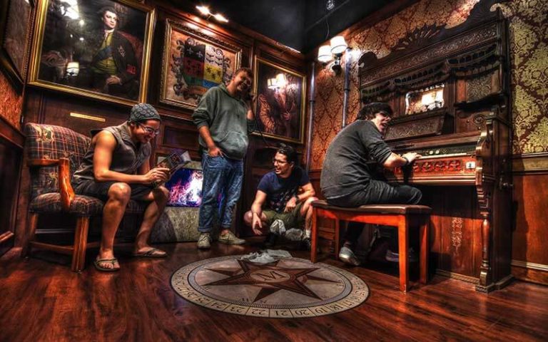 young men in a museum themed room with piano discussing clues at escapology