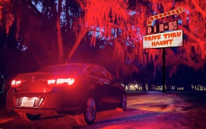 car driving along spooky dark path in woods with drive thru haunt sign