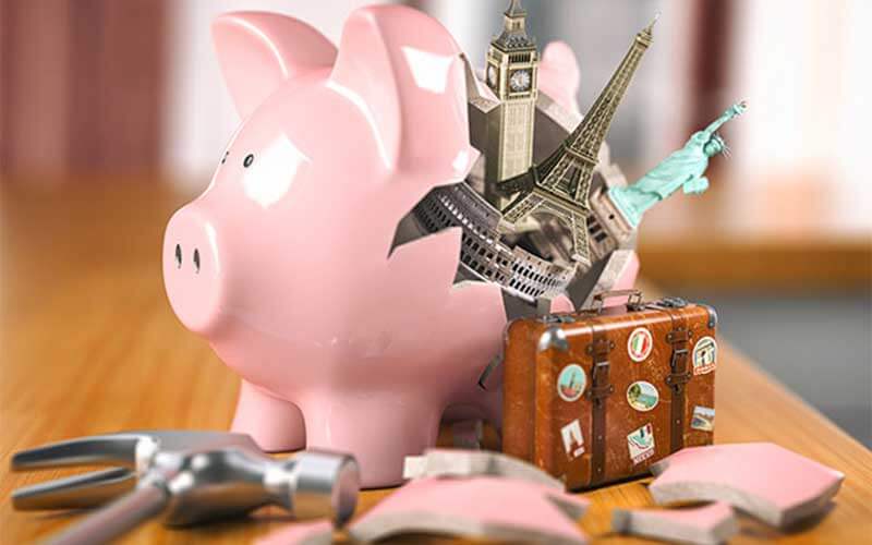broken piggy bank with eiffel tower luggage and big ben and statue of liberty popping out of it 