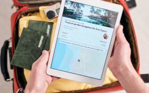 ipad with travel info held over suitcase with passports and camera