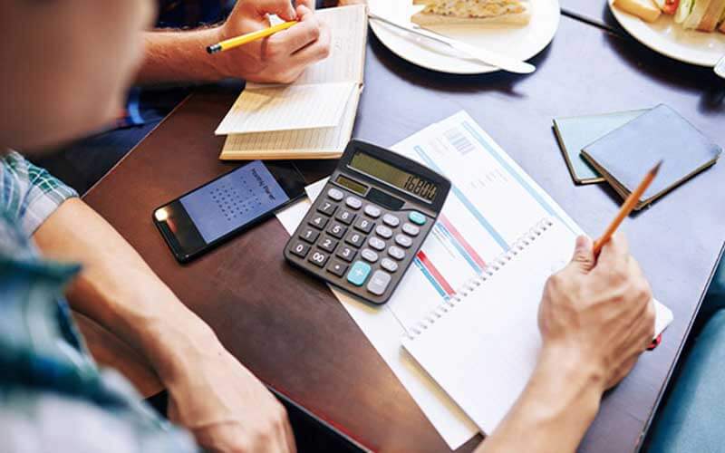 calculator, assorted documents, a sandwich and a notepad on a table next to sandwiches