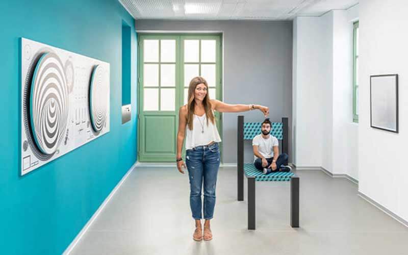 blue and white optical illusion room with woman standing next to chair with seemingly miniature man at museum of illusion icon park