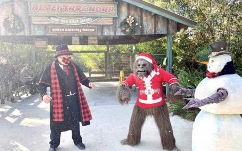 gentleman dressed in holiday outfit next to swamp ape wearing santa outift and a snowman