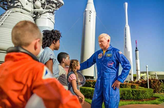 astronaut speaks with kids with the rocket garden behind at kennedy space center visitor complex for real florida adventures