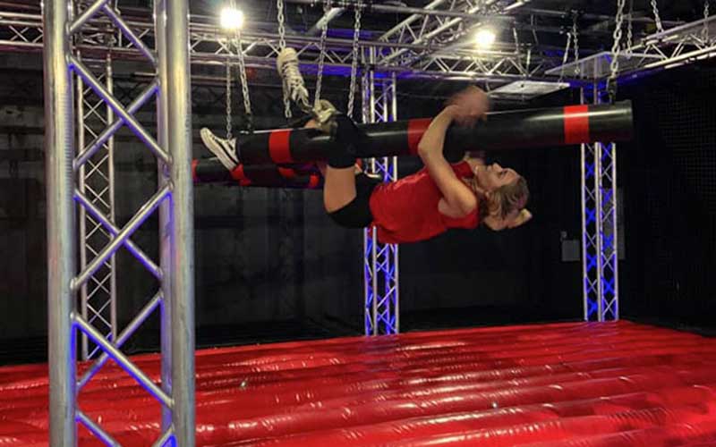 athletic woman climbs along hanging padded obstacle course at xtreme ninja challenge