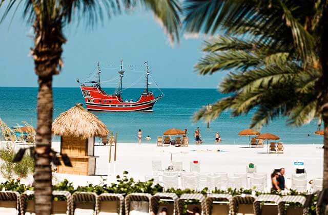 group on a beach with palm trees huts umbrellas and a red pirate ship in blue water at clearwater beach for real florida adventures