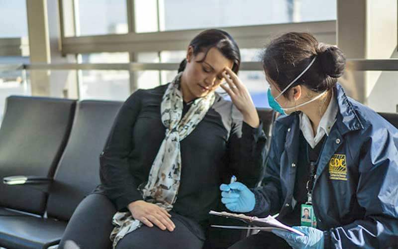 woman in airport rests head on fingers while speaking with cdc officer