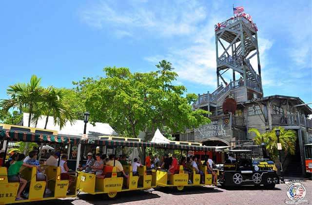 conch tour train parked below tower and trees at shipwreck museum key west