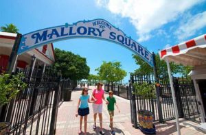 family walking under a welcome sign gate from the waterfront area at mallory square market key west