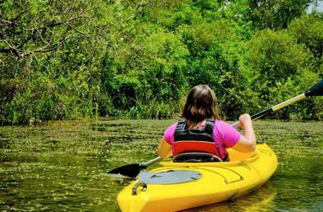 girl in a yellow kayak rowing along river with thick brush at rainbow springs state park dunnellon florida