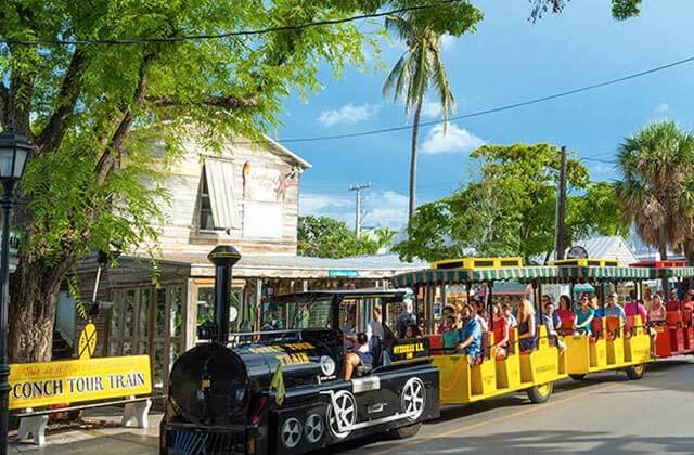locomotive themed tram with yellow and red cars leaving tour office at conch tour train key west