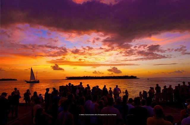 orange and pink cloudy sunset over the water with a sailboat and crowd silhouettes at mallory square market key west