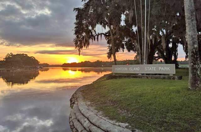 shoreline with park sign and sunset over water at hontoon island state park deland florida