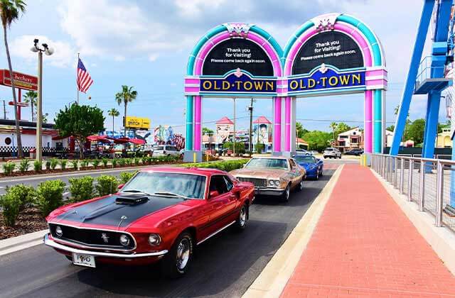 row of classic cars driving through the main street gateway for old town car show saturdays