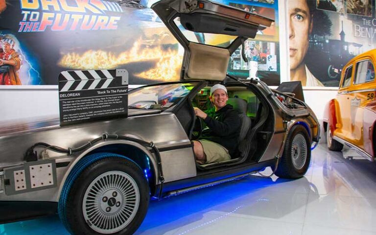 smiling man seated in delorean car in exhibit at orlando auto museum at dezerland park