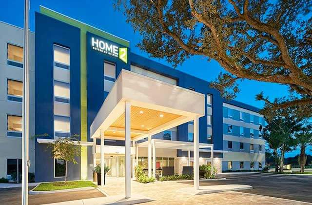 blue and green hotel building at night with drop off entrance and trees at home2 suites by hilton palm bay i-95